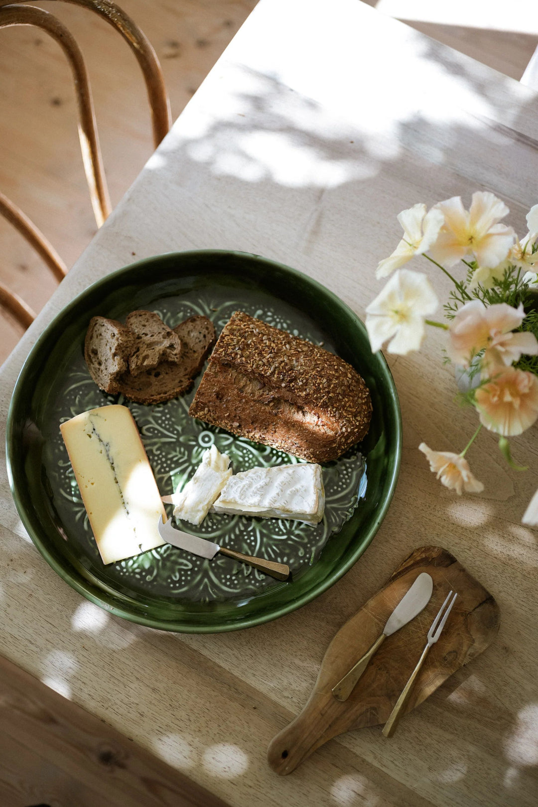 Green ceramic plate with bread and cheese on a wooden table with flowers.