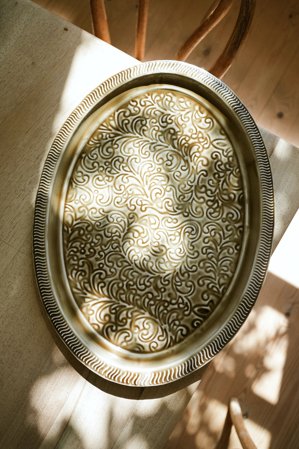 Decorative oval metal tray with intricate patterns on a wooden surface