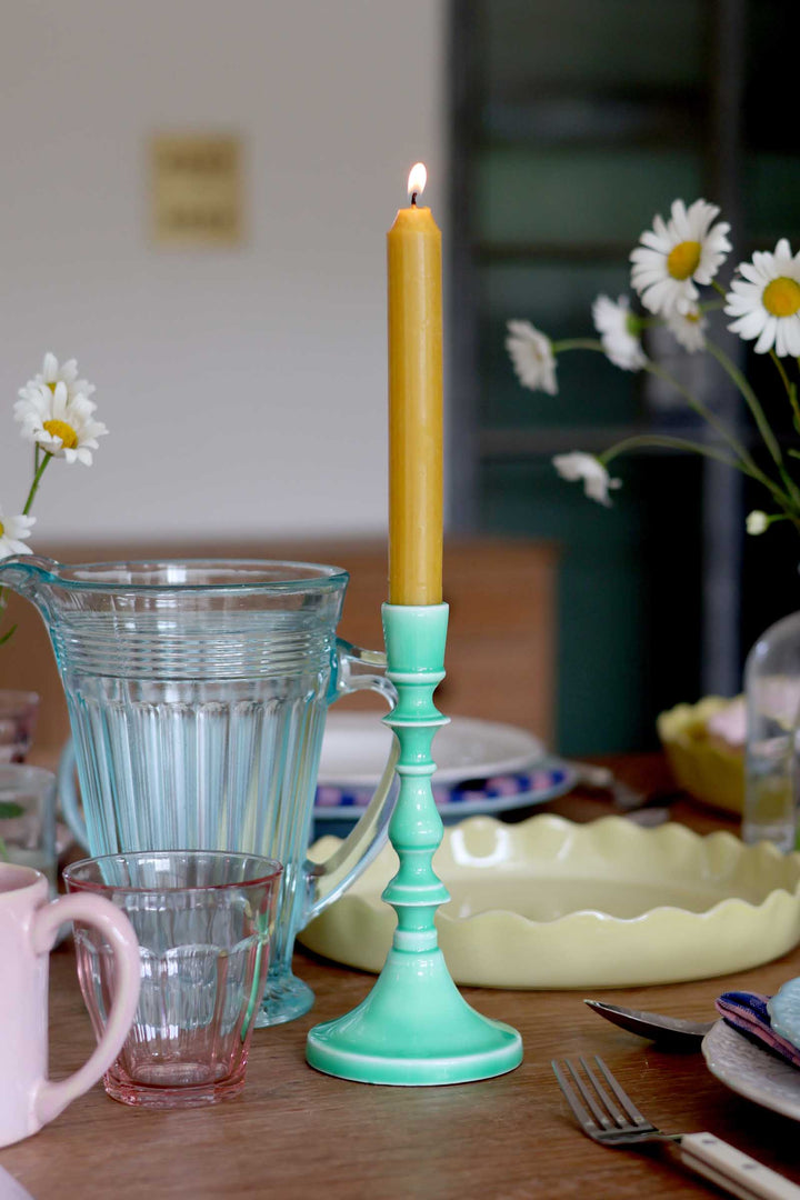 Teal candle holder with a lit yellow candle on a table with glasses and flowers.