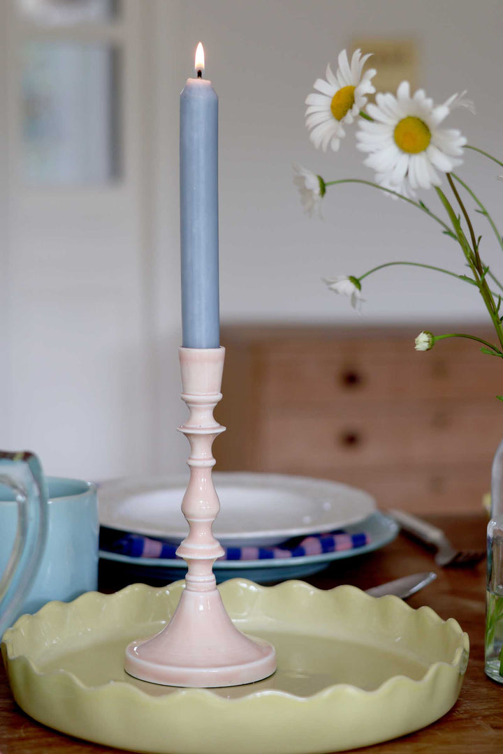 Candle in a decorative holder on a table with plates and flowers in the background