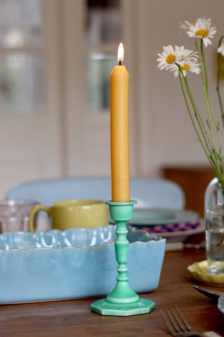 Yellow candle in a green holder on a table with a blurred background