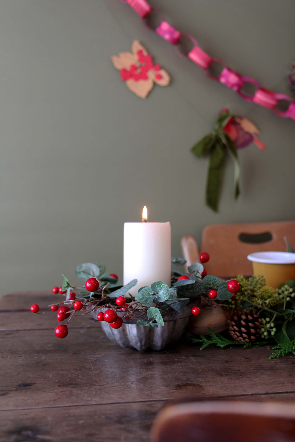 Decorative candle with berries on a wooden table against a neutral wall with festive decorations.
