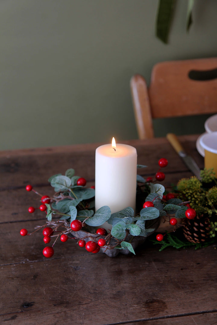 Candle with red berries and greenery on a wooden table