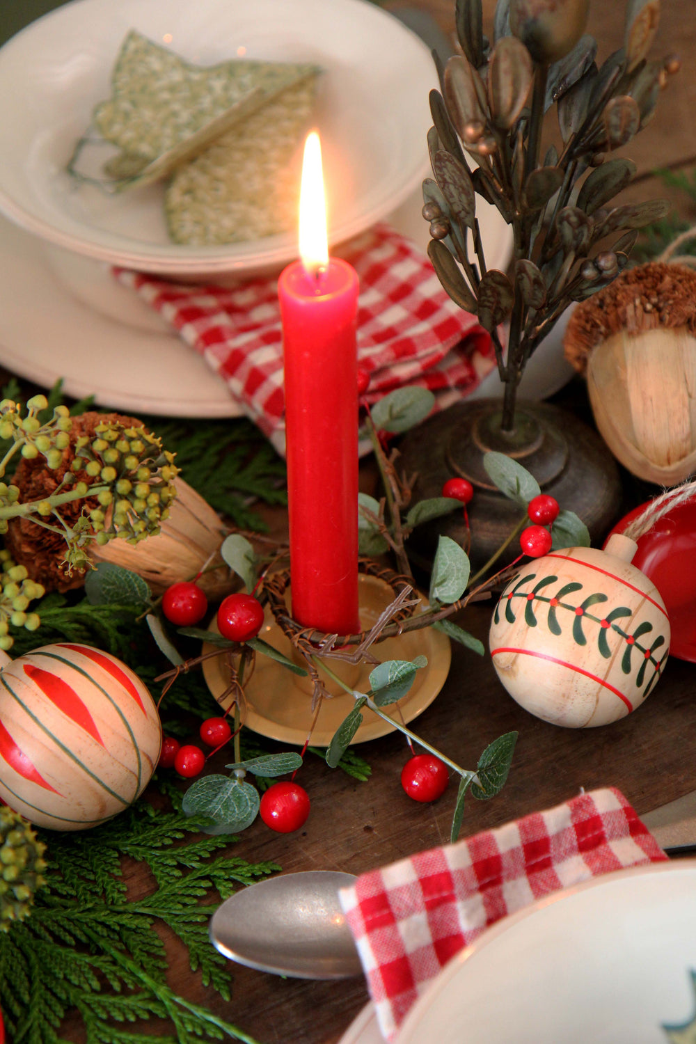 Decorative table setting with a red candle, Christmas ornaments, and greenery.
