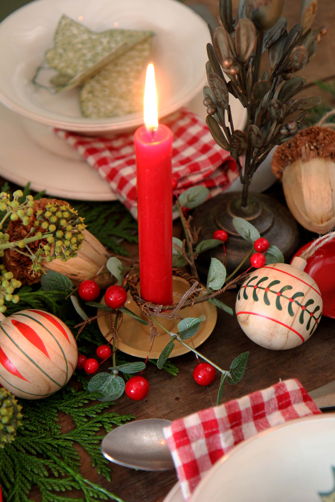 Decorative table setting with a red candle, Christmas ornaments, and greenery.