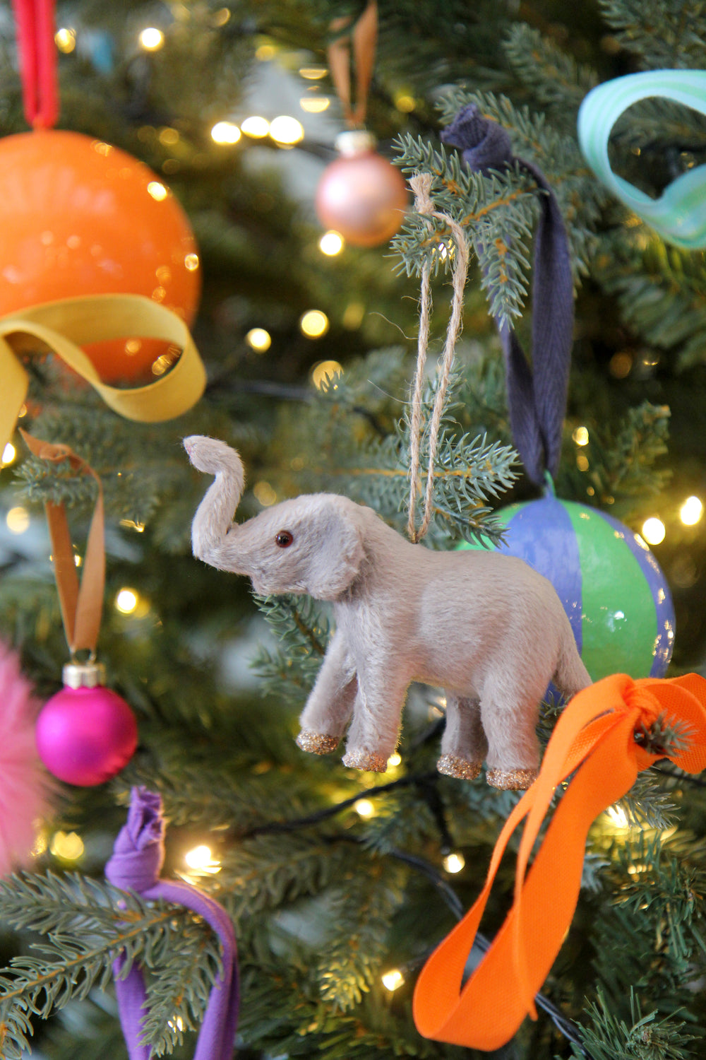 Plush elephant toy hanging on a decorated Christmas tree with colorful ornaments.