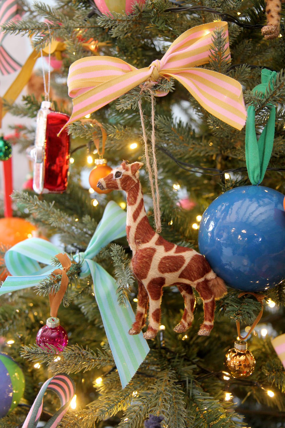 Decorative Christmas tree with colorful ornaments including a giraffe figure, blue ball, and pink ribbon.