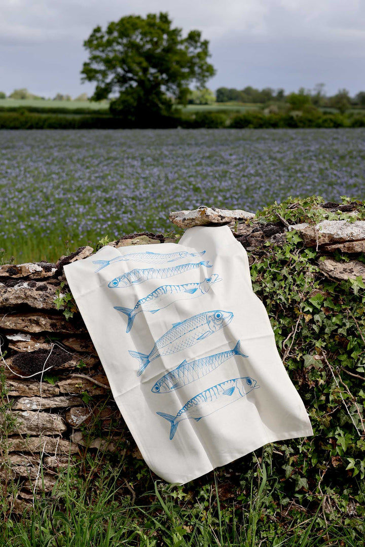 Tea towel with fish design on a stone wall with a field and trees in the background