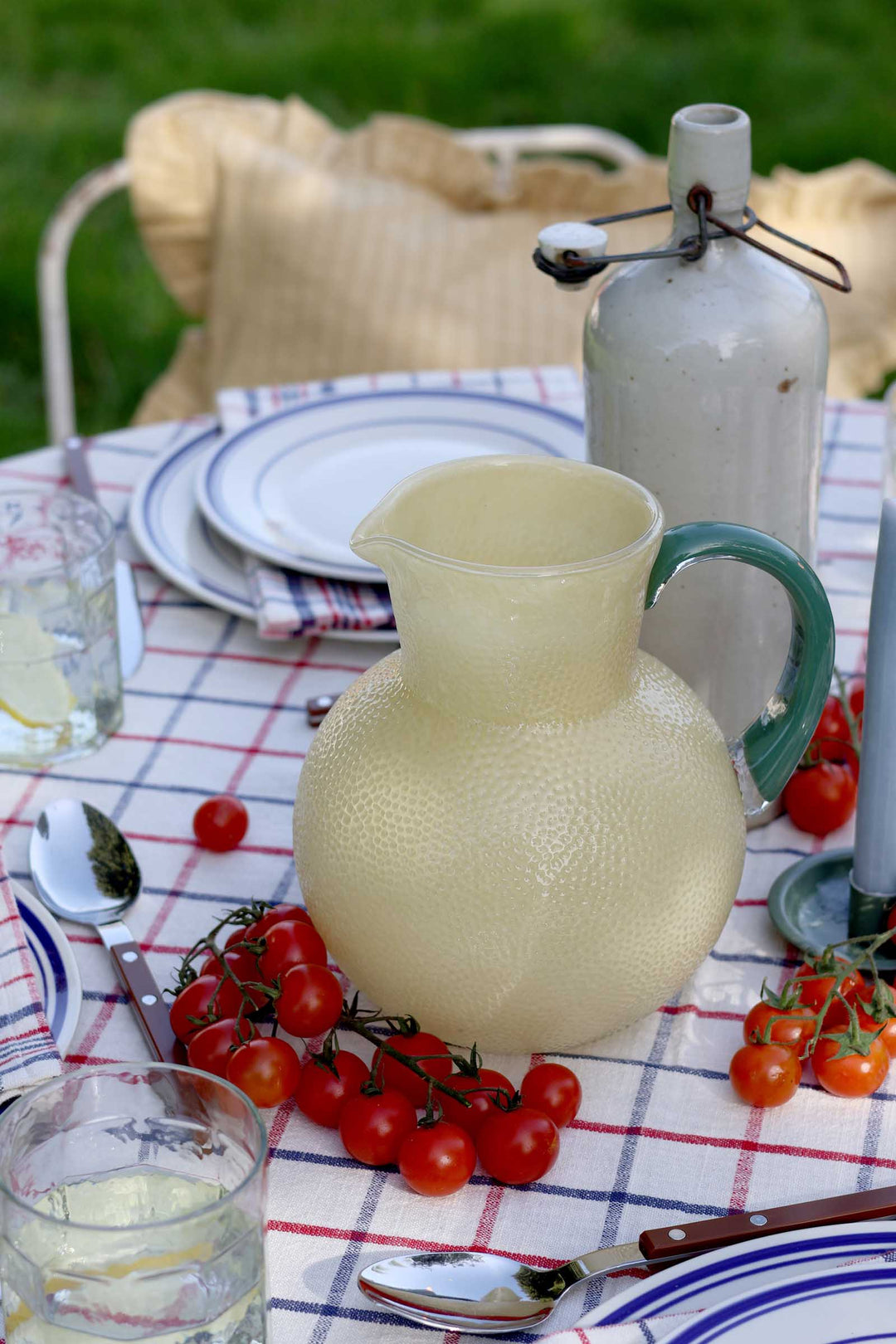 Yellow pitcher on a table with red tomatoes and a checkered tablecloth