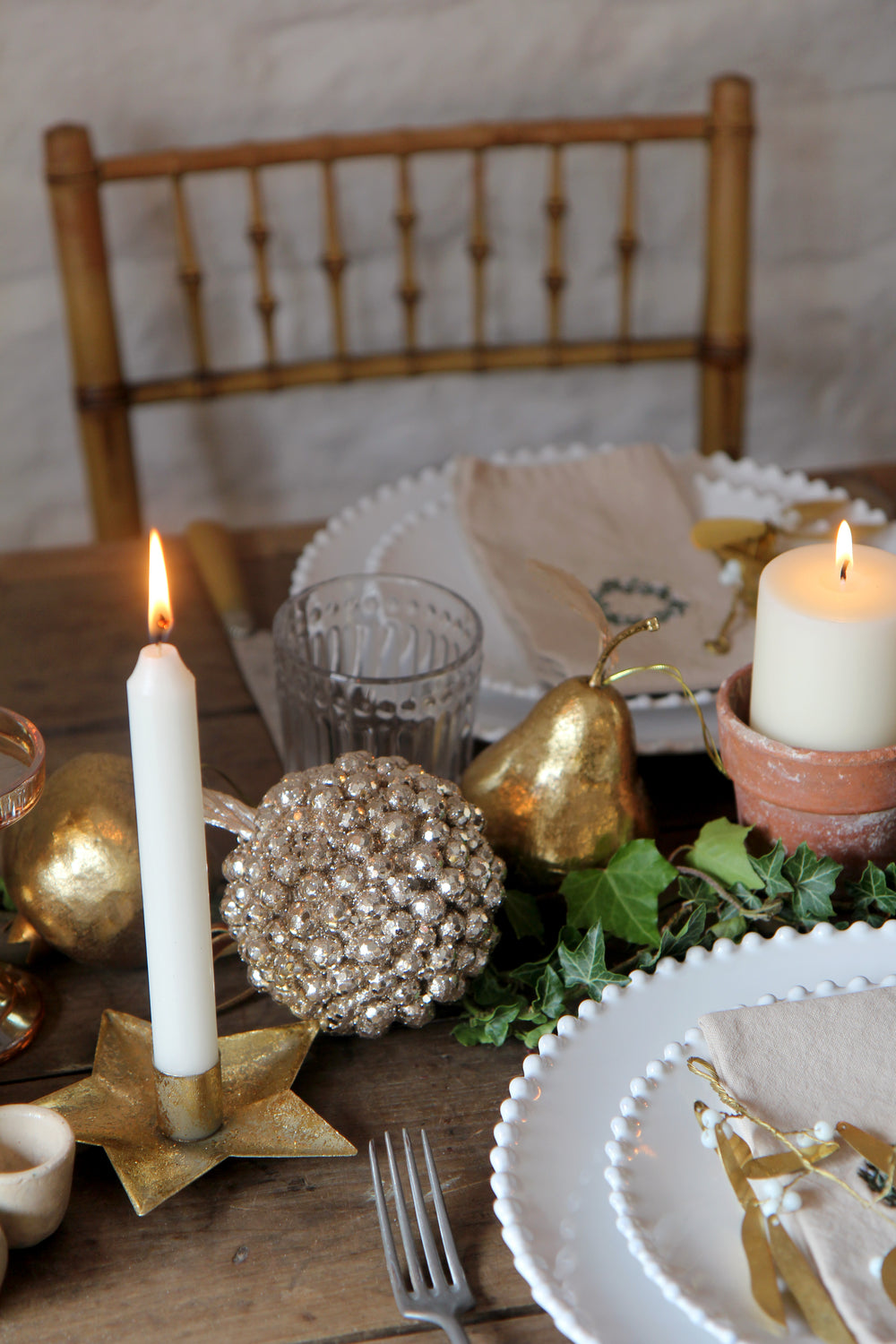 Decorative table setting with candles, gold ornaments, and greenery on a wooden table.