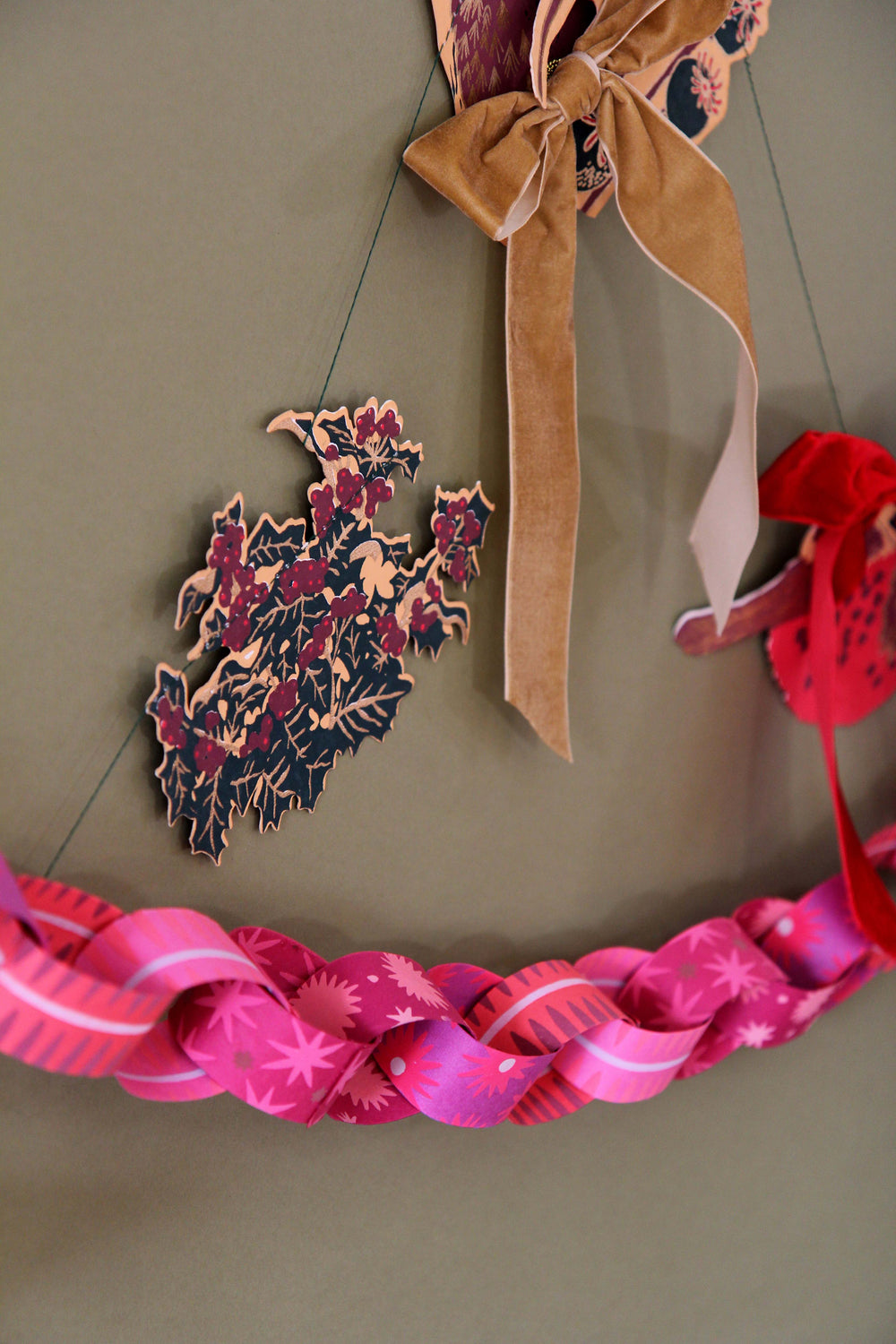 Decorative wreath with pink ribbons and floral patterns on a plain background. Gold bow