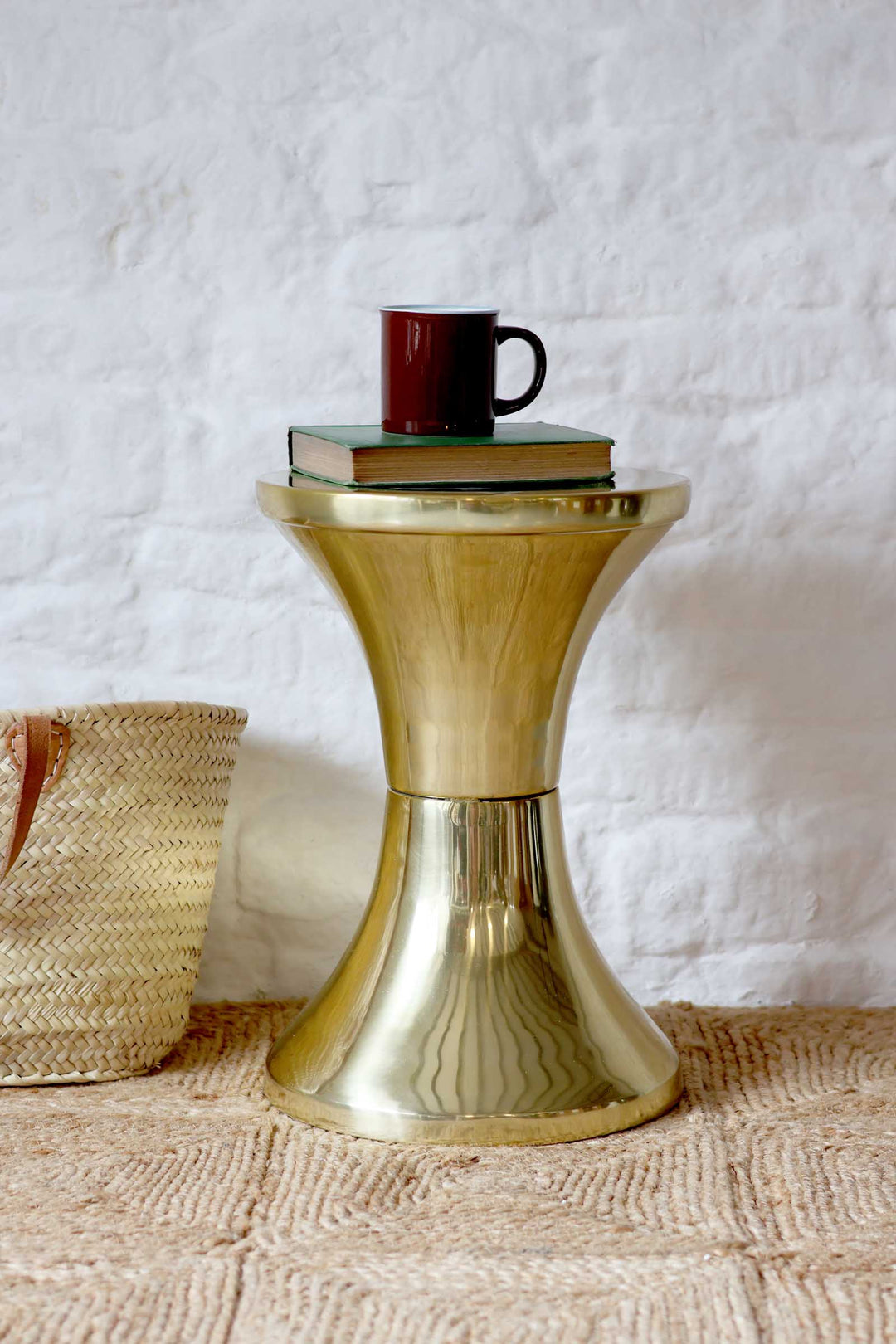 Gold side table with a red mug and books on a textured surface and white wall background