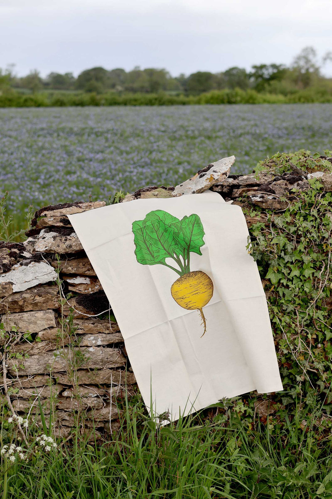 White towel with a green and yellow radish illustration on a stone wall with a natural background