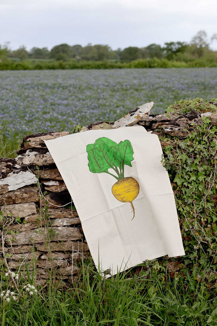 White towel with a green and yellow radish illustration on a stone wall with a natural background