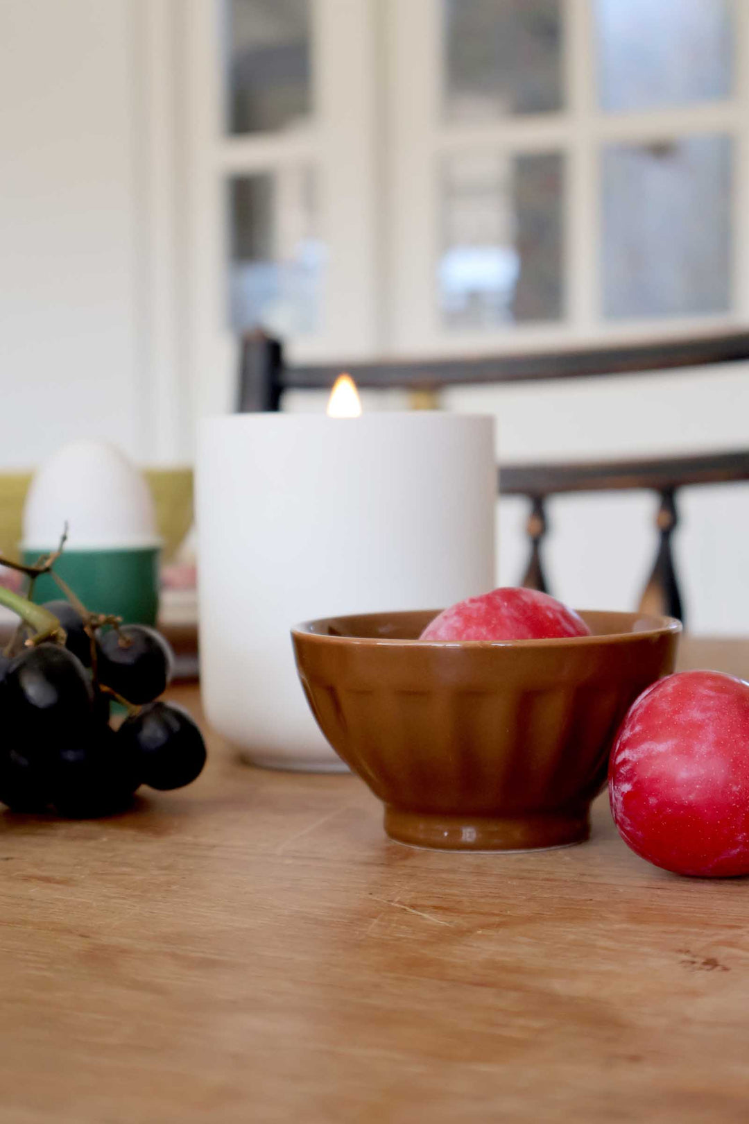 Candle, bowl with radishes, and grapes on a wooden surface.