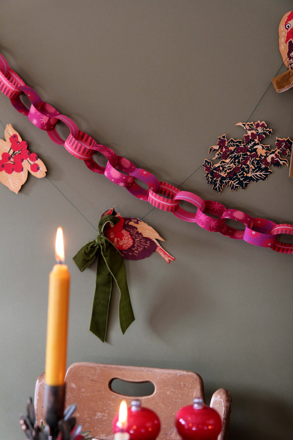 Decorative chain with festive elements on a wall, including a candle and small ornaments.