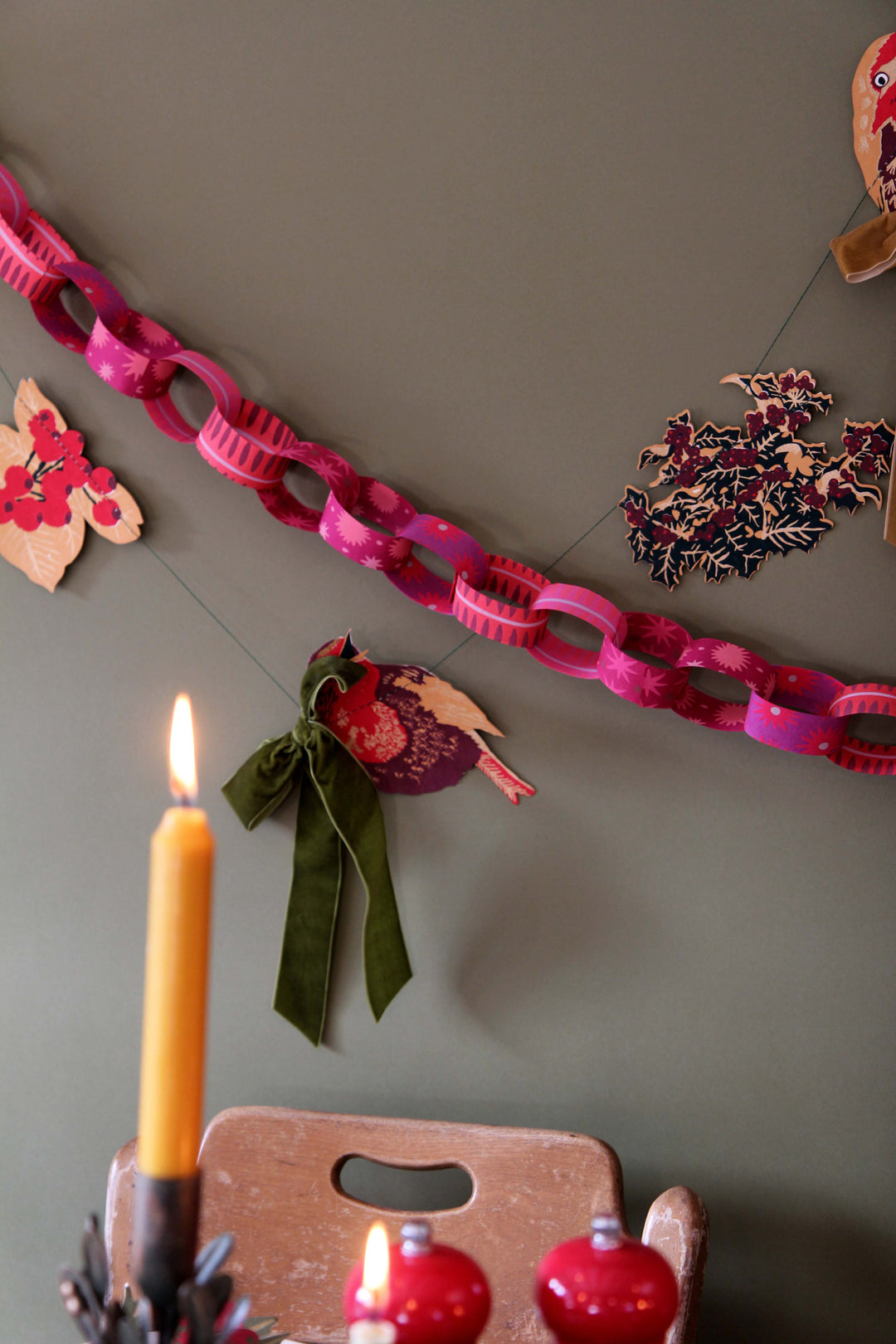 Decorative chain with festive elements on a wall, including a candle and small ornaments.