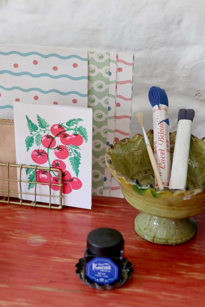 Ink bottle, notebooks, and markers on a wooden surface with a white background