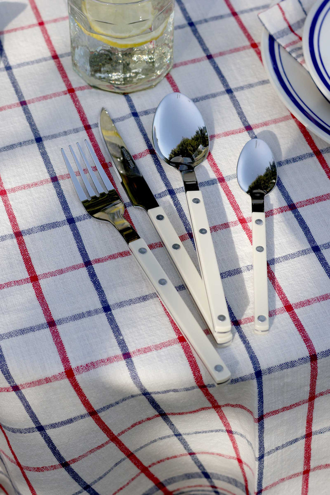 Set of cutlery including a fork, knife, and two spoons on a checkered tablecloth.