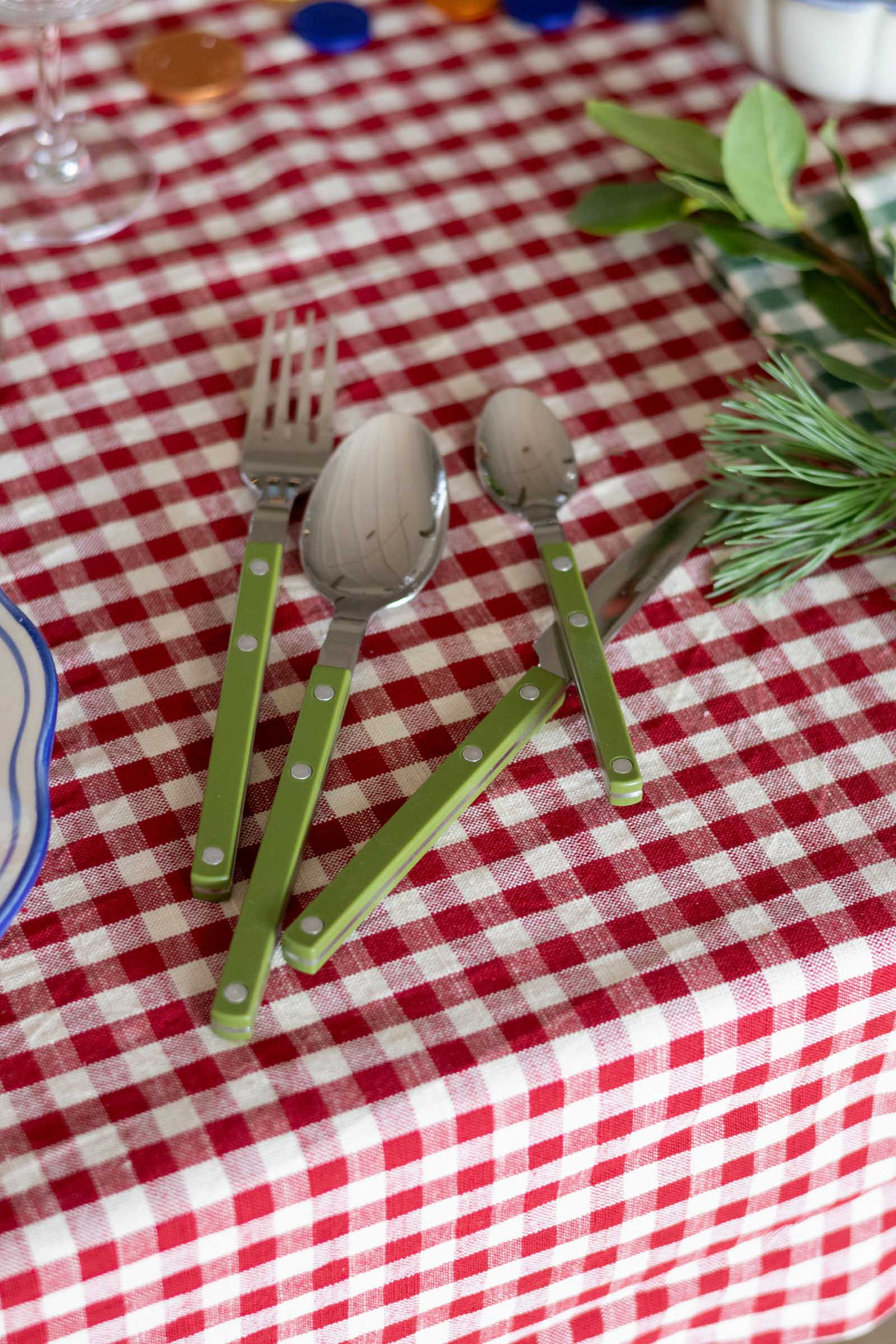Green-handled children's cutlery, including a fork, spoon, and knife, arranged on a red and white checkered tablecloth.