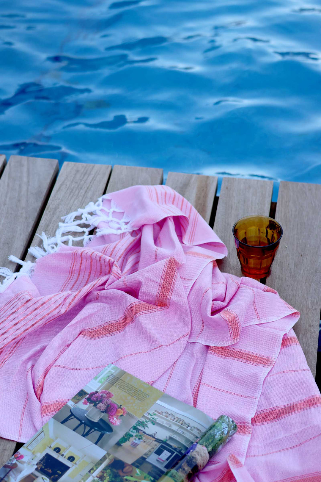 Pink towel and magazine on a wooden deck by a pool