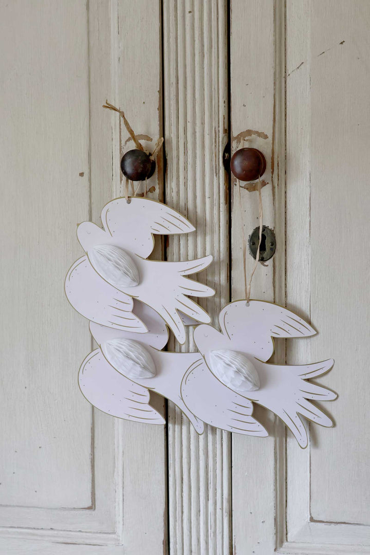 Three white wooden dove ornaments with wings and small white bead accents, hanging on a distressed off-white wooden door.