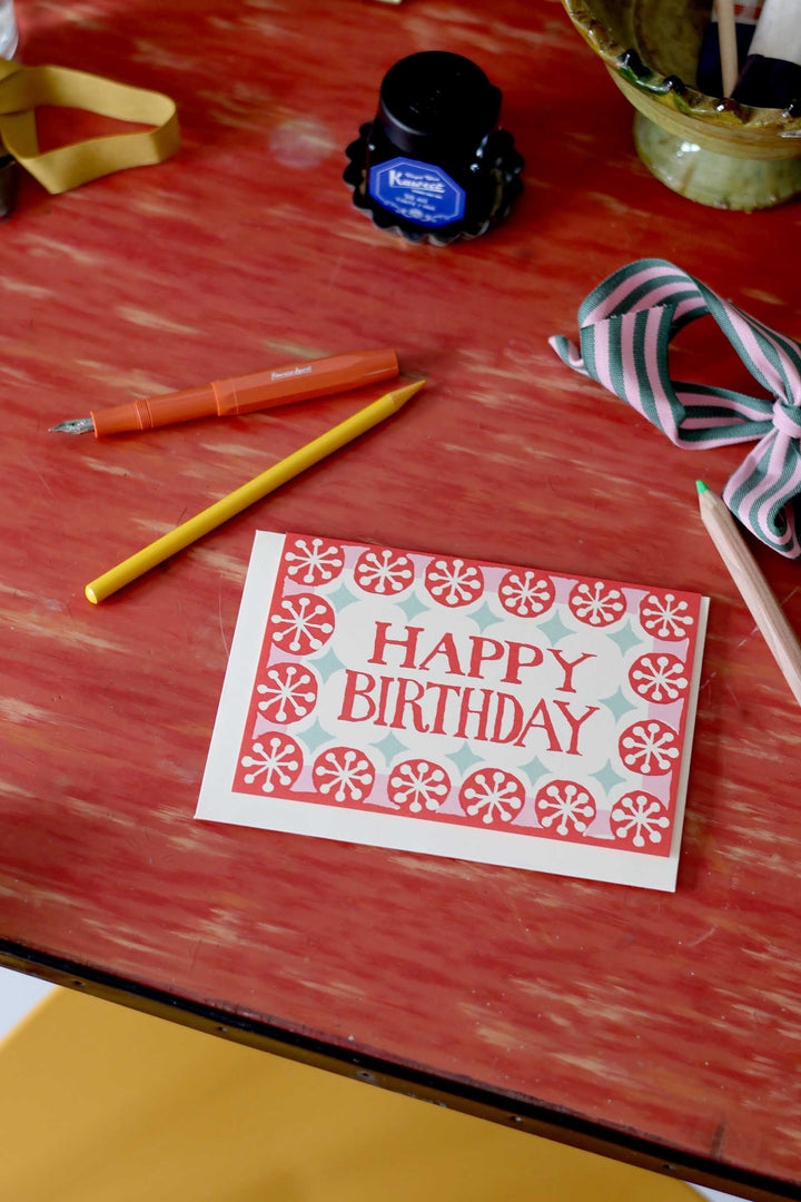 Happy Birthday card on a red surface with writing utensils