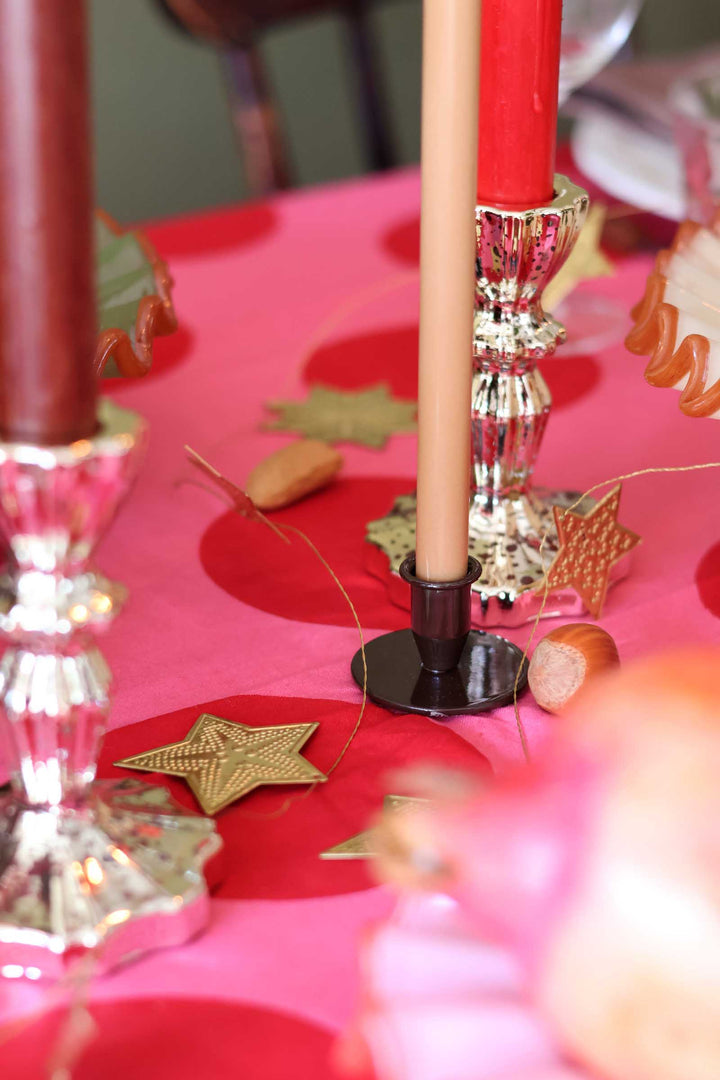 A close-up of a festive table centerpiece with a pink tablecloth, red candles in silver candlesticks, gold star decorations, and cork accents.