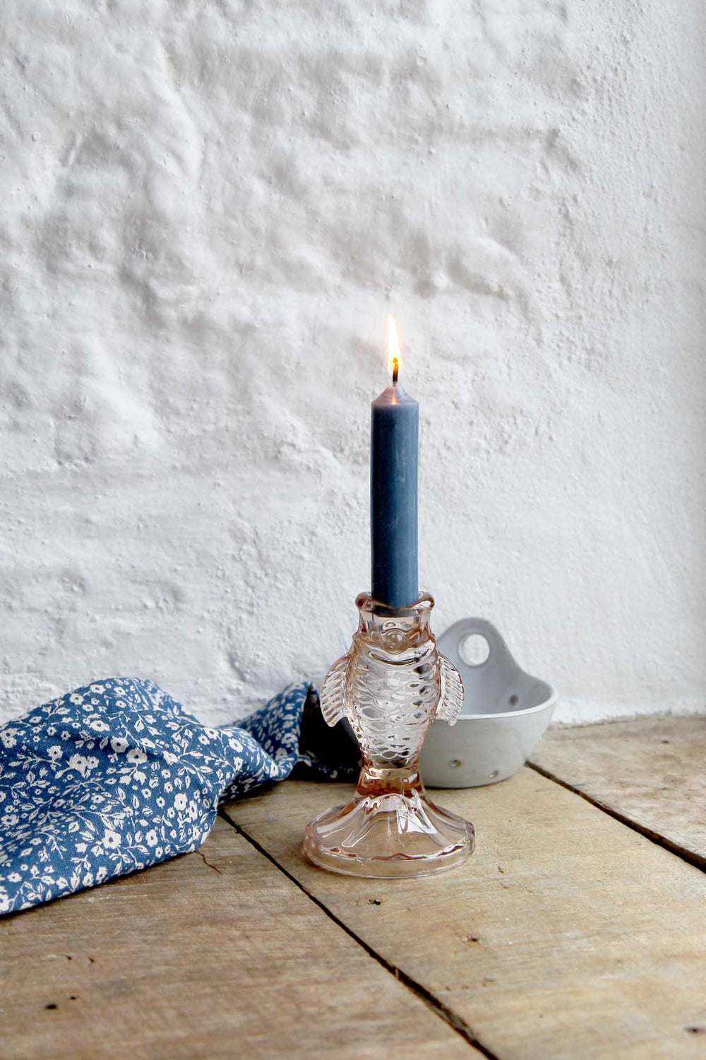 Candle in a decorative glass holder on a wooden surface with a white textured wall background