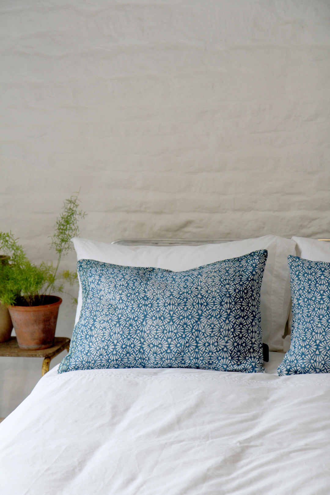 oblong vintage sari kantha cushions with blue block print design pictured on bed with white bed linen