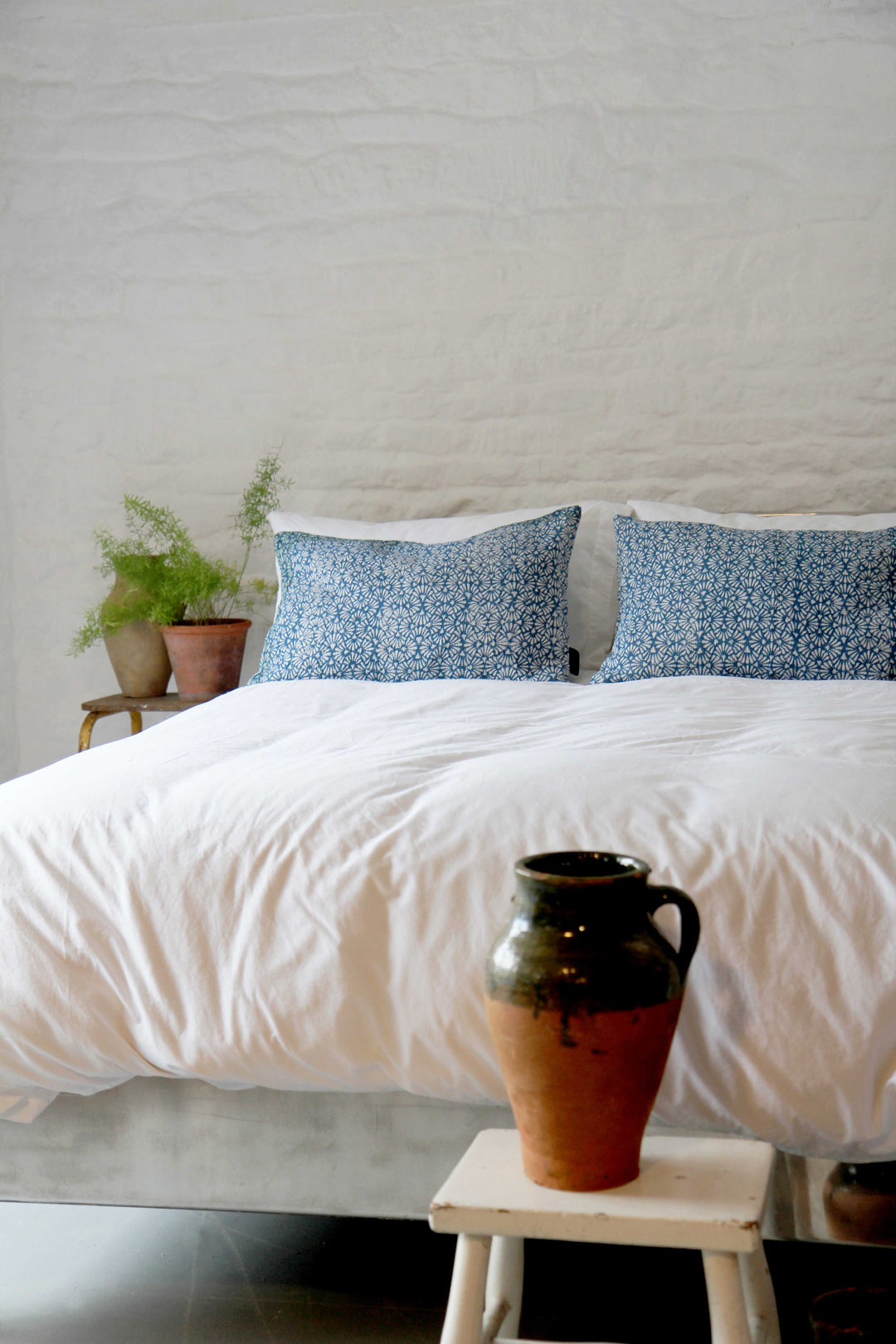 calm white bedroom with vintage olive pot and two oblong vintage sari kantha cushion on bed