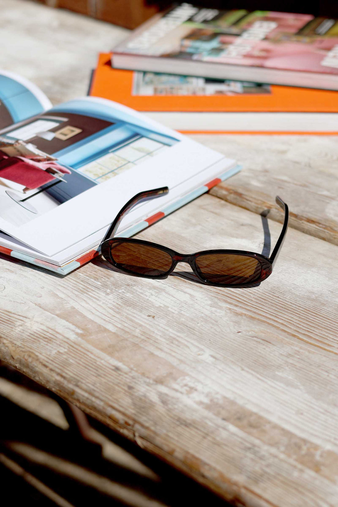 Sunglasses on a wooden surface with an open book and magazines in the background