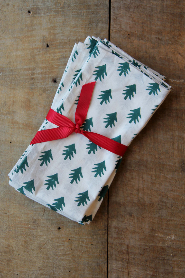 Folded napkins with green tree pattern tied with red ribbon on a wooden surface