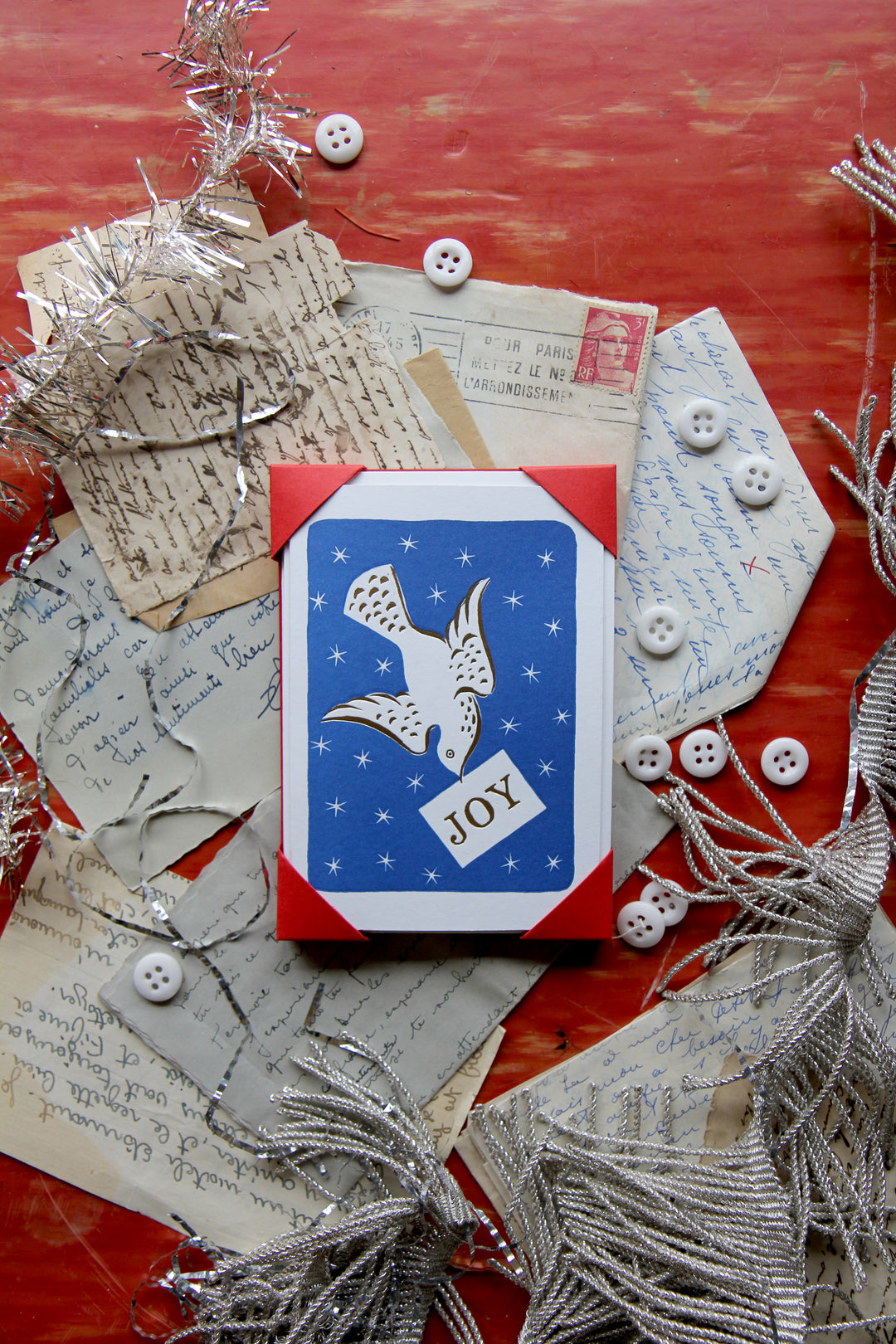 Decorative card with an eagle design and 'JOY' text, surrounded by festive elements on a red surface.
