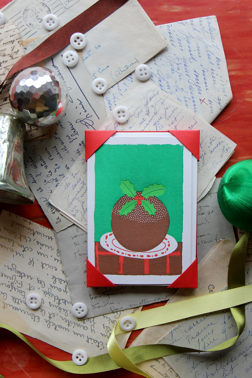 Card with Christmas pudding design on a textured surface with ribbons and buttons.