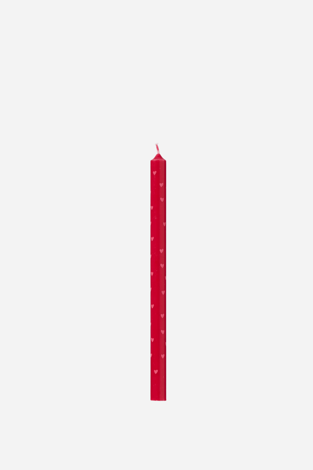 A single red taper candle with small white heart patterns, shown vertically against a plain light gray background.