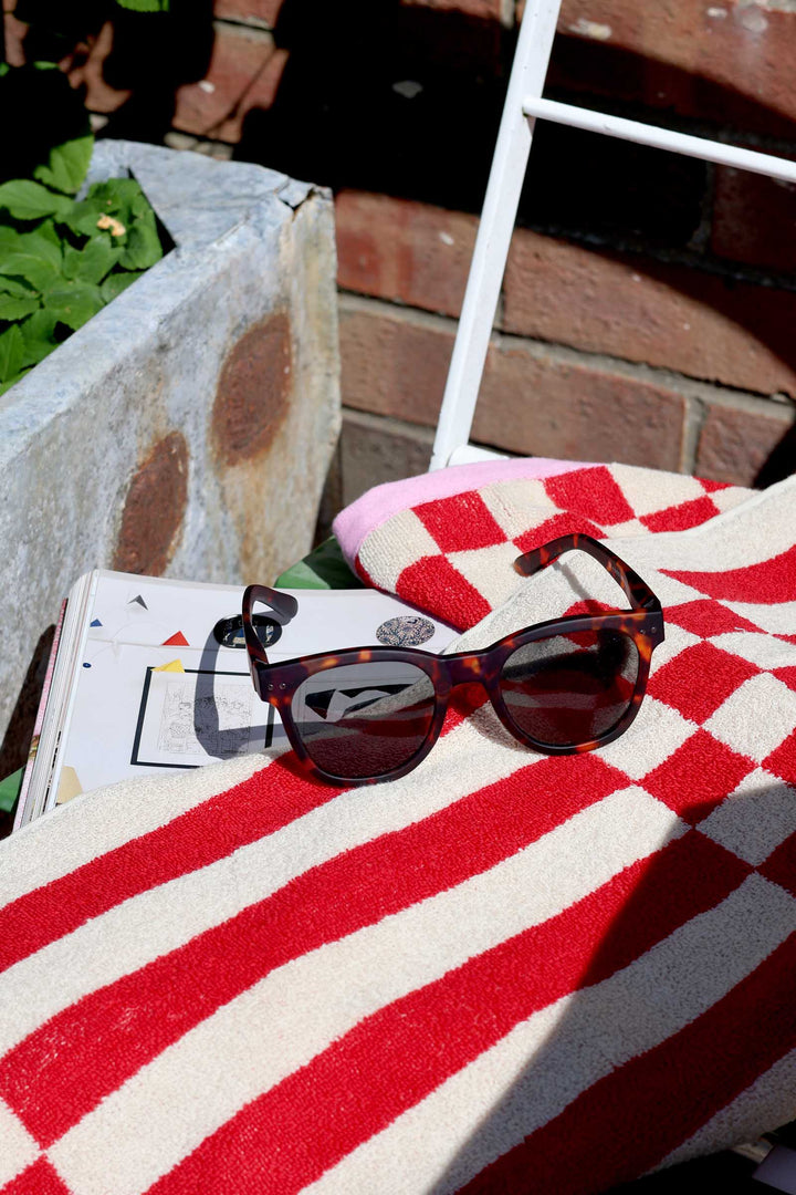 Sunglasses on a red and white checkered towel with a magazine underneath