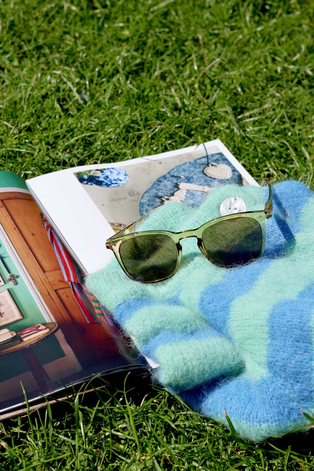 Sunglasses on a blue blanket with an open book on grass