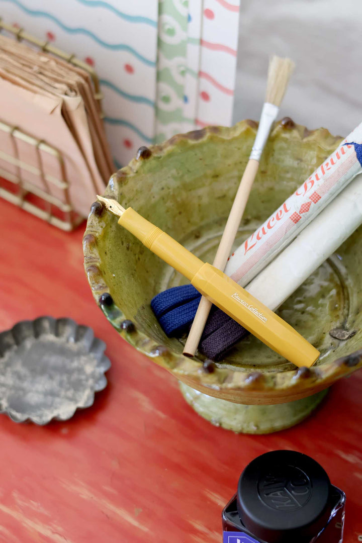 Green ceramic container with markers and a candle on a red surface