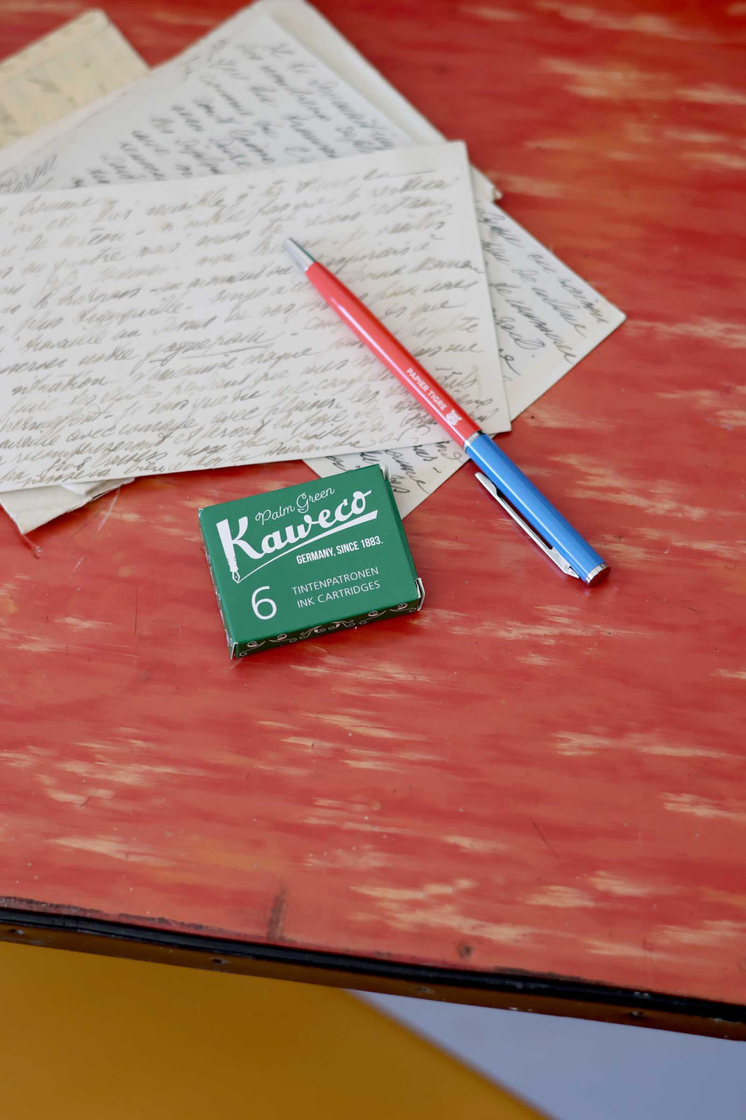 Kaweco pencil and green case on a red surface with handwritten paper