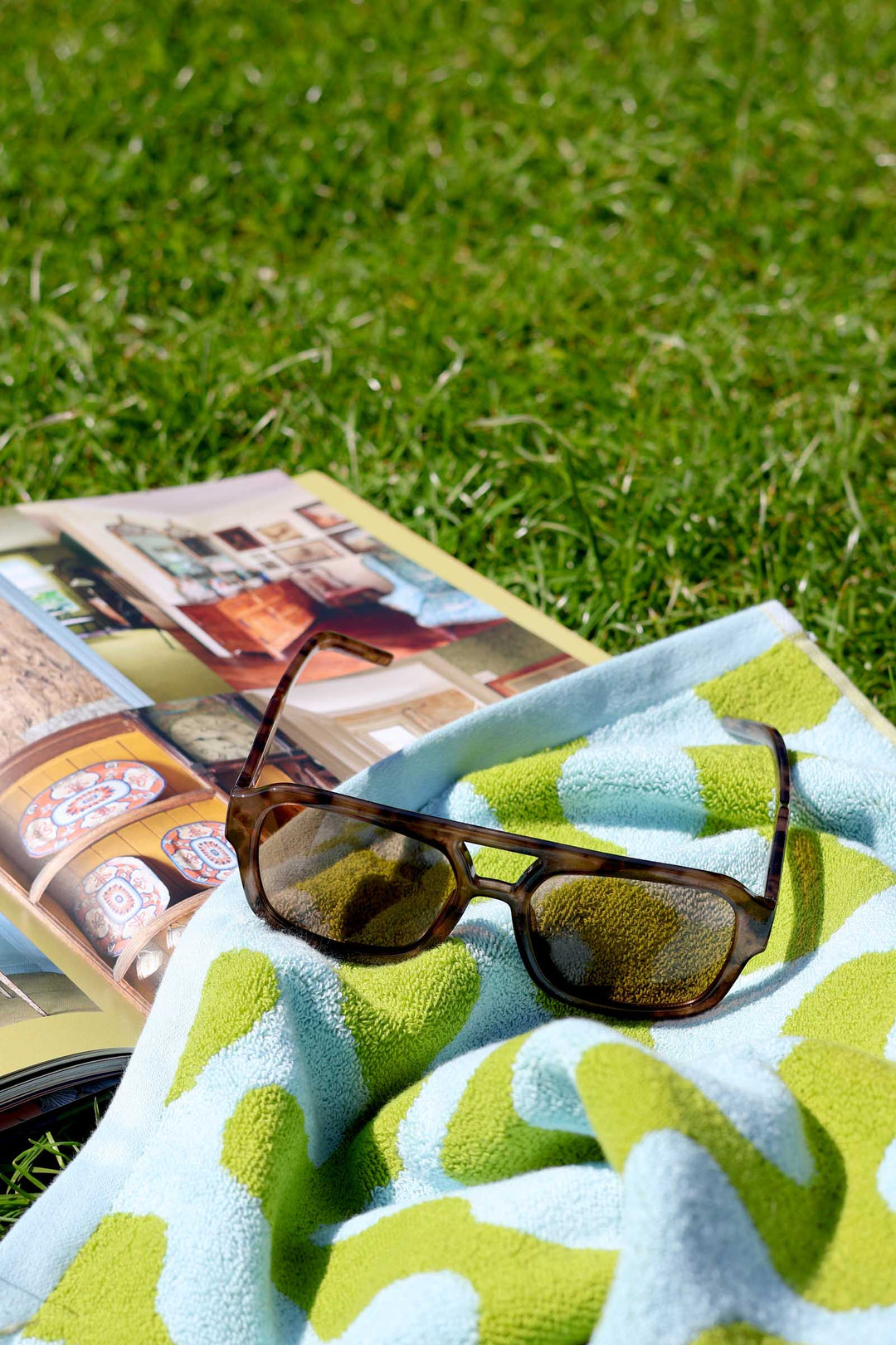 Sunglasses and a book on a green towel with grass in the background