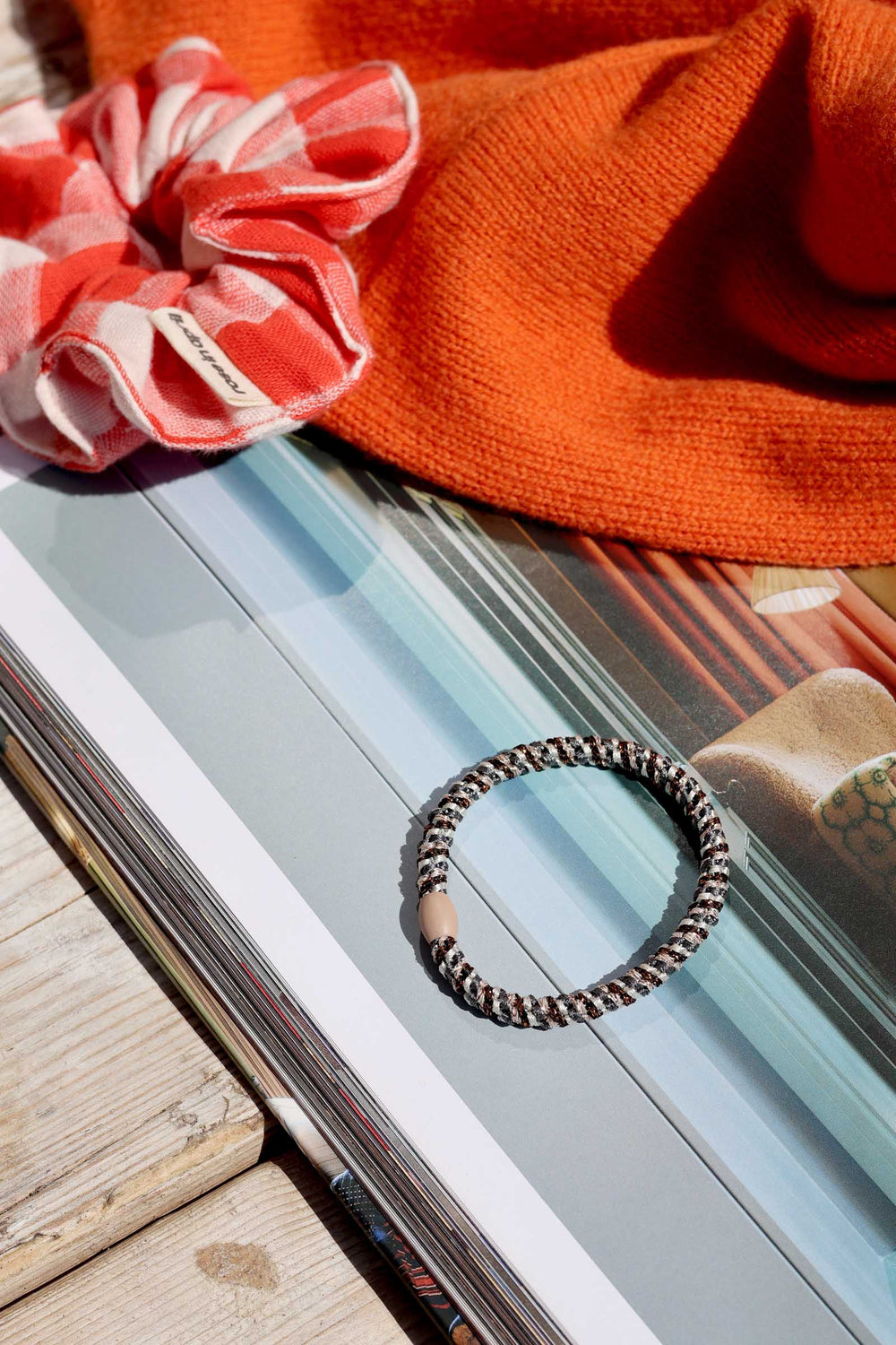Bracelet on a magazine with a pink scrunchie and orange fabric in the background
