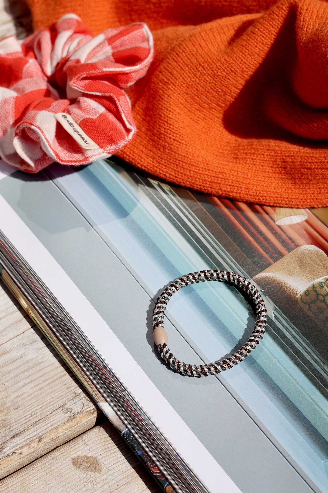 Bracelet on a magazine with a pink scrunchie and orange fabric in the background