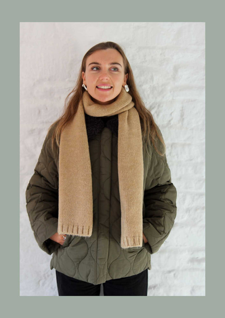 Person wearing a beige scarf and green jacket against a white background