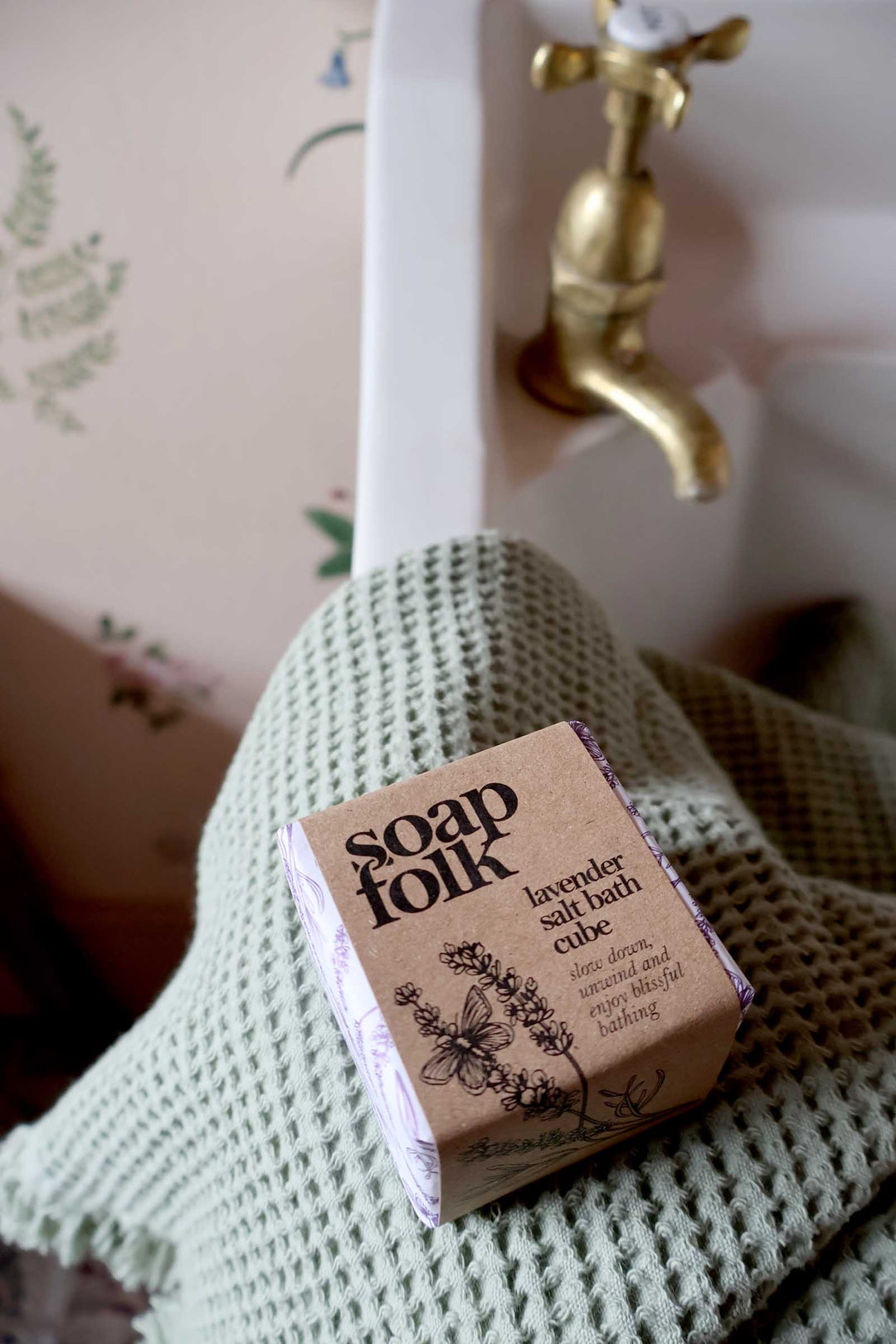 Bar of soap with 'Soap Folk' packaging on a textured towel in a bathroom setting.