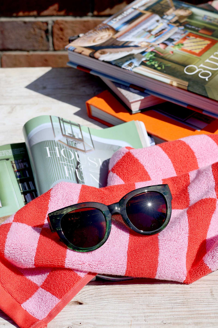 Sunglasses on a red and white checkered towel with books in the background