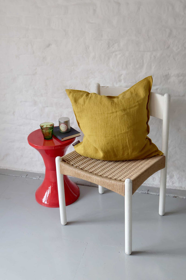 Chair with a yellow cushion next to a red side table against a white wall.