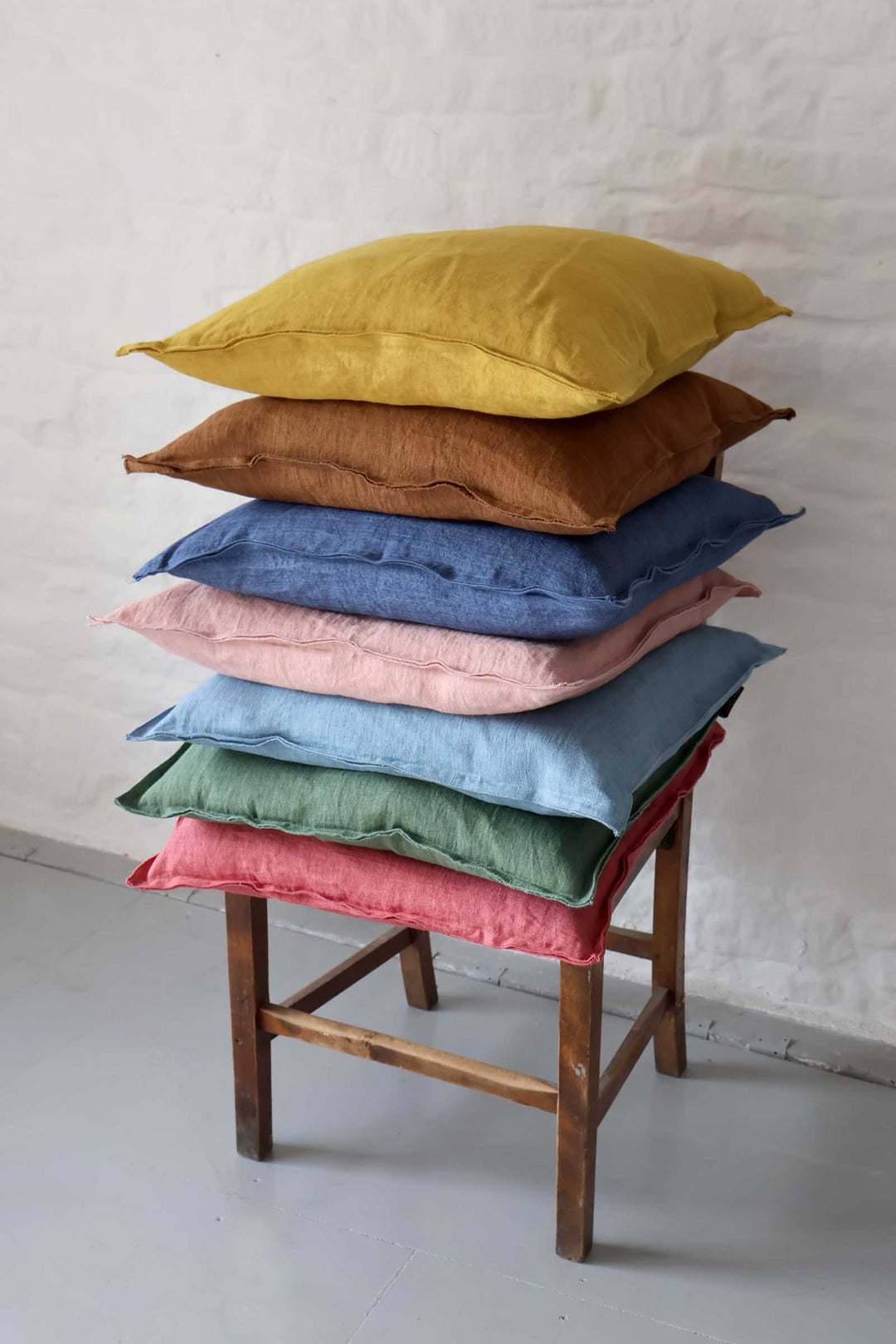 Stack of colorful pillows on a wooden chair against a white wall.