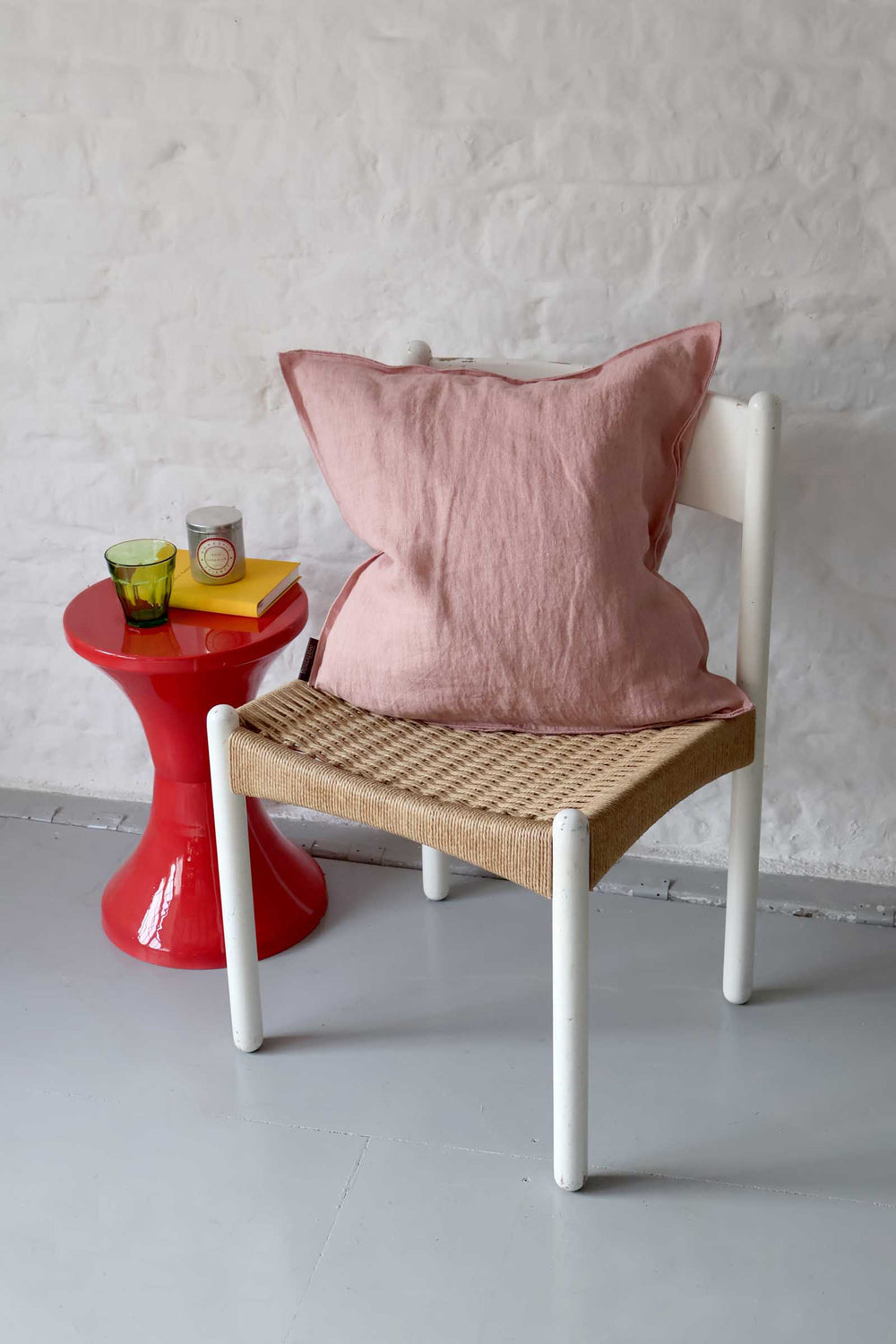 Chair with a pink pillow next to a red side table against a white wall.