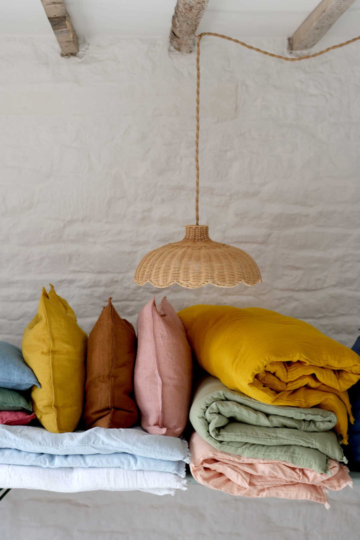 Colorful pillows and blankets under a woven pendant light against a white wall.